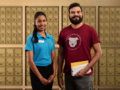 The UPS Store associate standing with a smiling customer holding mail, in front of The UPS Store mailboxes