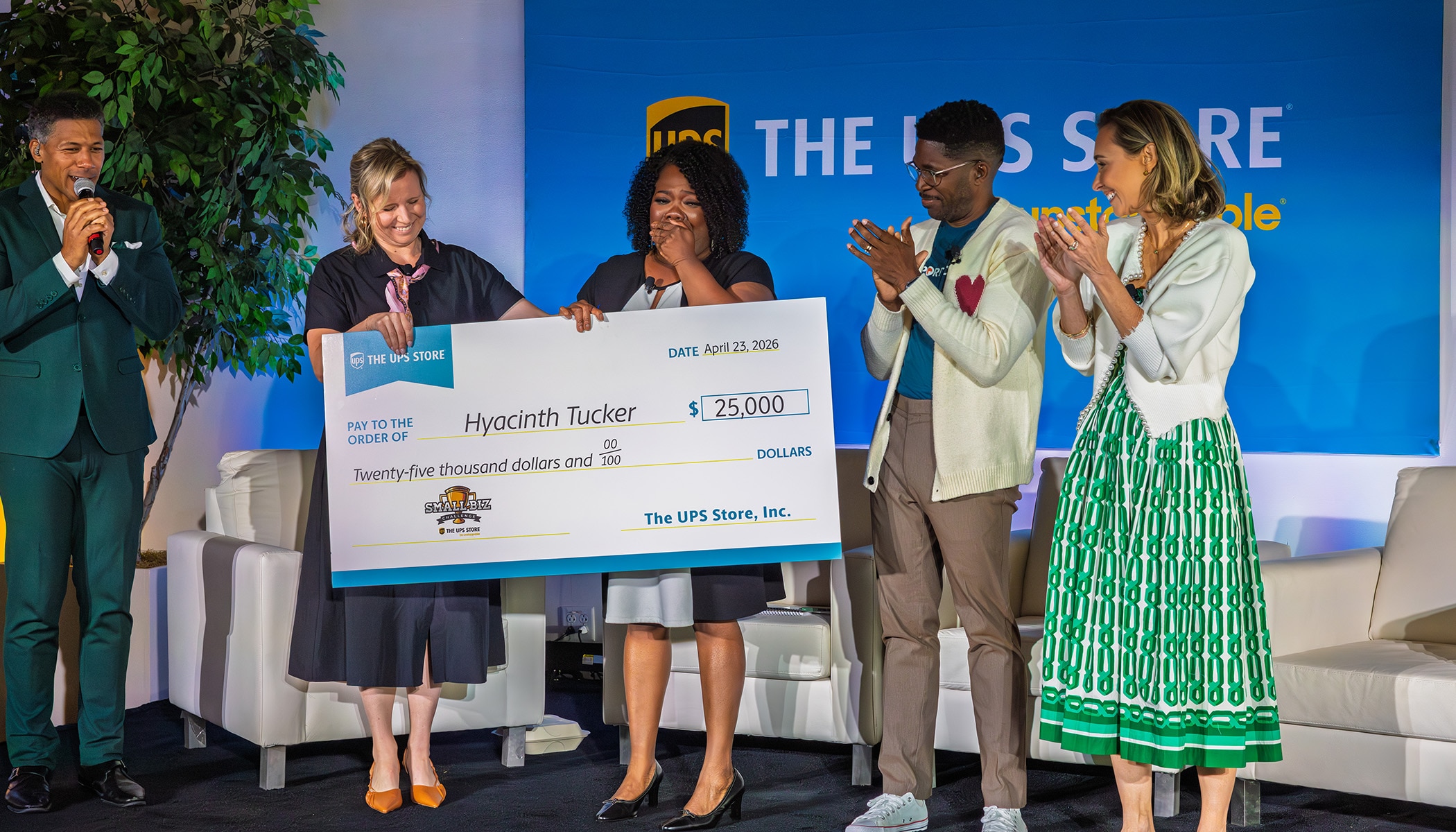Group of people standing on stage applauding a woman holding a check