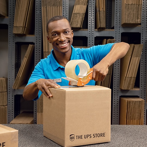 A male The UPS Store asssociate taping a box closed