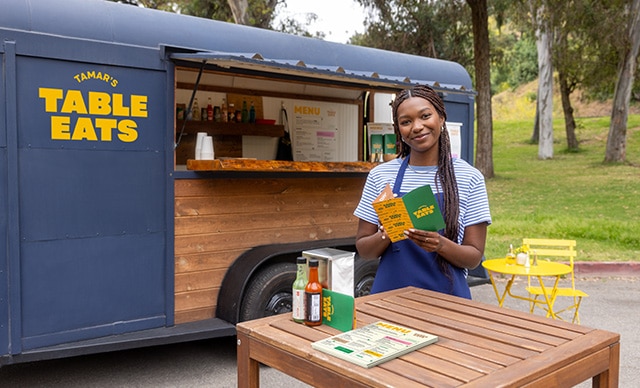 A small business owner holding printed materials outside of their food truck